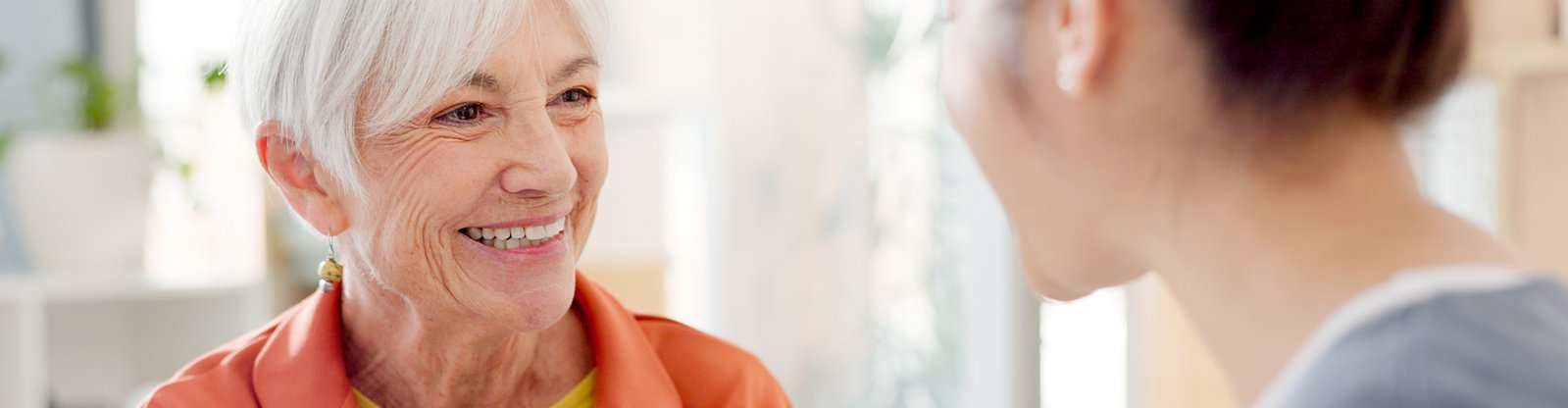 AdobeStock_816117366 Seniorin lächelt Pflegekraft an. Beide geben sich vertraut die Hand.